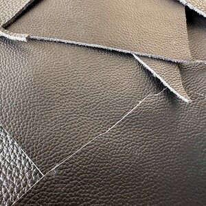May include: Close-up of black leather with a textured surface. The leather is folded over itself, creating a layered effect.