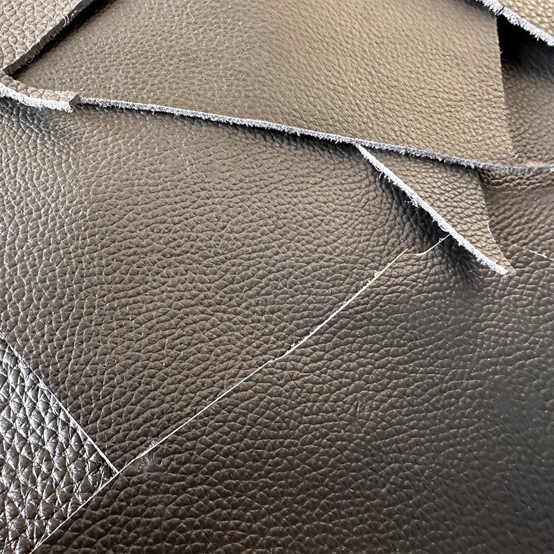 May include: Close-up of black leather with a textured surface. The leather is folded over itself, creating a layered effect.