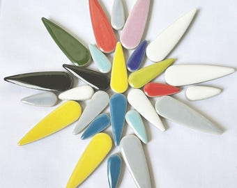 Puede incluir: Una colección de azulejos cerámicos de forma de lágrima de colores, incluyendo amarillo, rojo, azul, verde, negro, blanco y gris.