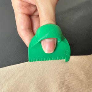 Pode incluir: Ferramenta de polegar de plástico verde com uma borda serrilhada, projetada para ajudar com costura e artesanato.