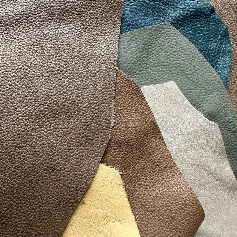 May include: A collection of leather swatches in various shades of brown, beige, gray, and blue. The swatches are arranged in a fan shape, with the darkest shade at the bottom and the lightest shade at the top.