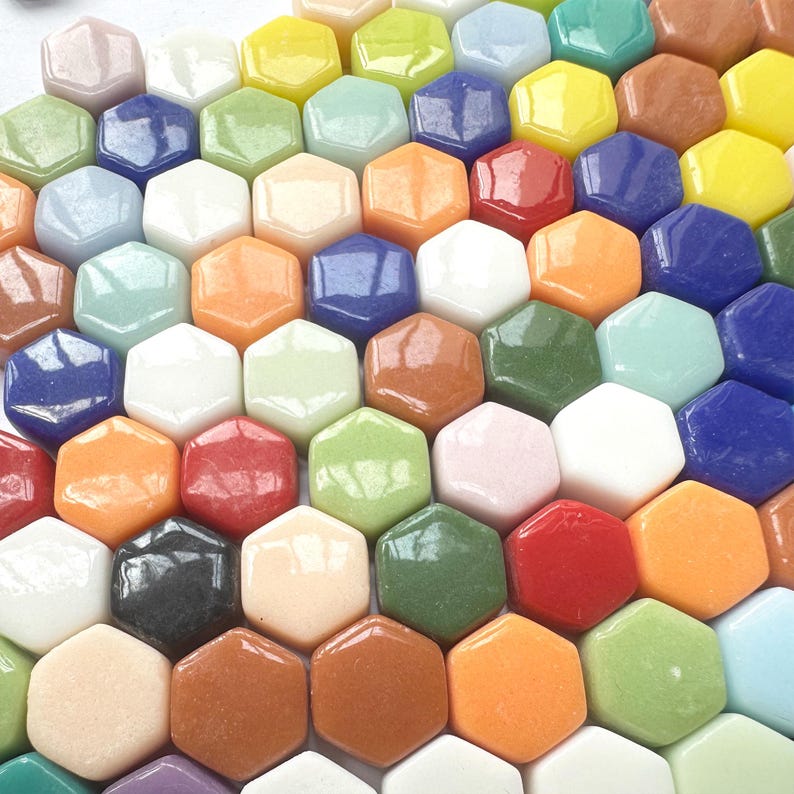 Pu&ograve; includere: Una collezione di piccole piastrelle esagonali in vetro liscio in una vibrante gamma di colori, tra cui rosso, arancione, giallo, verde, blu, bianco, nero e varie tonalit&agrave; pastello. Ogni piastrella presenta una finitura superficiale lucida.