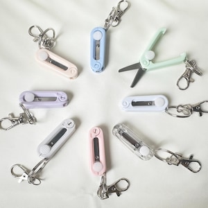May include: A set of nine pastel-colored keychain tools, including scissors, a utility knife, and a pencil sharpener. Each tool has a silver metal ring for attaching to a keychain.