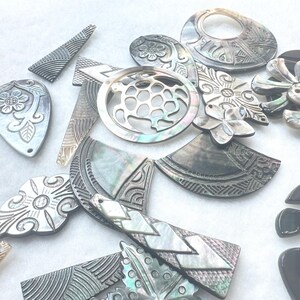 May include: A collection of iridescent mother-of-pearl shell pendants and charms in various geometric and organic shapes. The pieces feature intricate engraved patterns, including floral motifs, a turtle silhouette, and linear designs with a glossy finish.
