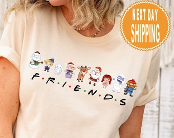May include: A beige t-shirt with a line of cartoon characters wearing Christmas attire. The characters are standing in a line and the text "FRIENDS" is written below them.