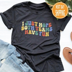 May include: Black t-shirt with the text "I just hope both teams have fun" in rainbow colors.