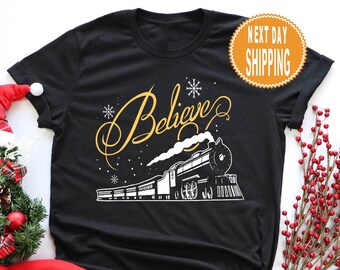 May include: Black t-shirt with a white train and the word "Believe" in gold lettering. The train is going through a snowy scene with snowflakes.