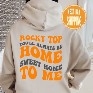 May include: A beige hoodie with the text "Rocky Top You'll Always Be Home Sweet Home To Me" in orange and grey lettering.