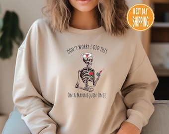 May include: Beige sweatshirt with a skeleton wearing a nurse's hat and holding a syringe. The text on the sweatshirt reads "Don't worry I did this on a mannequin once."