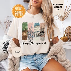 May include: Ivory-colored t-shirt featuring a colorful graphic of Walt Disney World landmarks. The design includes images of a castle, and other park features. The words "Walt Disney World" are printed below the graphic. The shirt has short sleeves and a crew neck.