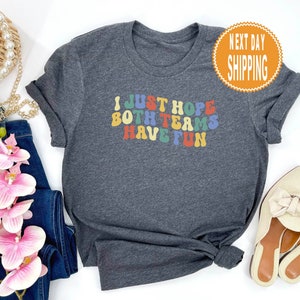 May include: A dark grey t-shirt with the text "I JUST HOPE BOTH TEAMS HAVE FUN" in rainbow colored letters.