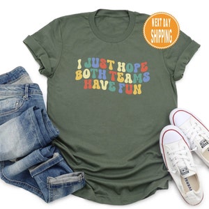 May include: A green t-shirt with the text "I just hope both teams have fun" in colorful retro font.
