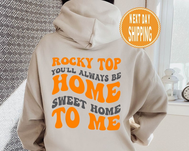 May include: A beige hoodie with the text "Rocky Top You'll Always Be Home Sweet Home To Me" in orange and grey lettering.