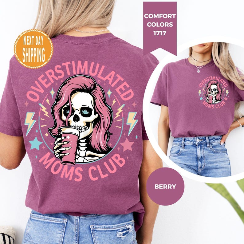 May include: Berry-colored t-shirt with a graphic featuring a skull with pink hair holding a pink cup, surrounded by text that reads "OVERSTIMULATED MOMS CLUB." The design includes stars and lightning bolts. The shirt has a round neck.