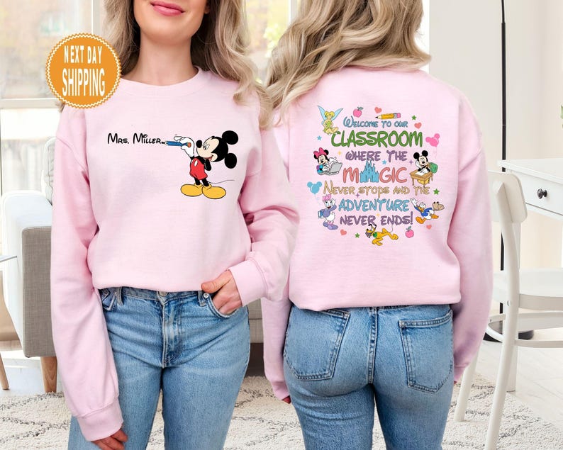 May include: Pink sweatshirt with a Mickey Mouse design on the front and a Disney-themed classroom quote on the back. The quote reads "Welcome to our classroom where the magic never stops and the adventure never ends!"