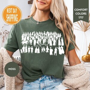 May include: Moss green t-shirt with a white graphic of a crowd of people and animals. The shirt has the words "Comfort Colors 1717" printed on it. The shirt is made of a soft material.