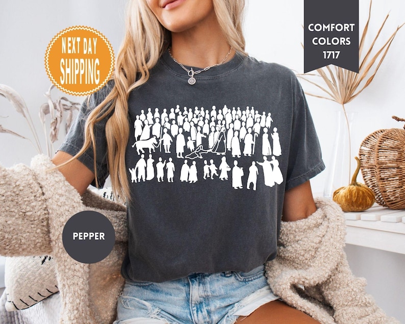 May include: Dark gray t-shirt with a white graphic of numerous silhouetted figures. The shirt has the text "COMFORT COLORS 1717" and "PEPPER" on it. The shirt is a crew neck and short-sleeved.