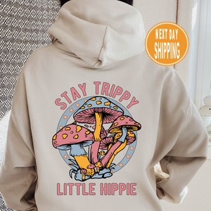 May include: A beige hoodie with a graphic of colorful mushrooms and the text "Stay Trippy Little Hippie".