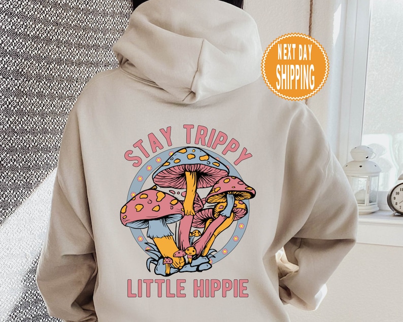 May include: A beige hoodie with a graphic of colorful mushrooms and the text "Stay Trippy Little Hippie".