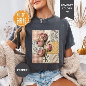 Może przedstawiać: Ciemnoszara koszulka z kwiatowym wzorem patchwork z różami. Koszulka ma napis "Comfort Colors 1717" i "Next Day Shipping". Widoczne jest również słowo "Pepper". Koszulka jest połączona z dżinsowymi szortami.