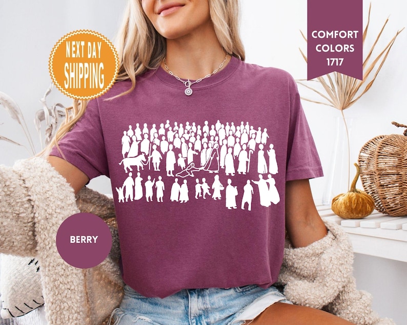 May include: Berry-colored t-shirt with a white graphic of numerous figures. The shirt has a crew neck and short sleeves. The words "Comfort Colors 1717" are in a burgundy rectangle. A round sticker says "Next Day Shipping".