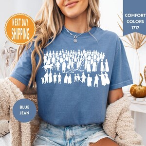 May include: Blue jean-colored t-shirt with a white graphic of a crowd of people. The shirt has the words "Comfort Colors 1717" on a blue banner. An orange circle with the words "Next Day Shipping" is also visible.