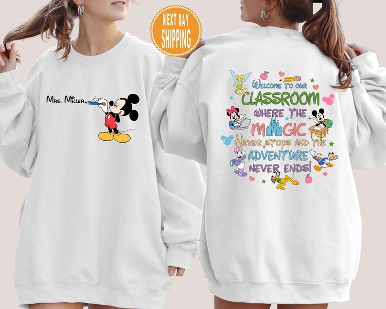 May include: White sweatshirt with a Mickey Mouse design and the text "Mrs. Miller". The back of the sweatshirt has a colorful design with Mickey Mouse and other Disney characters and the text "Welcome to our classroom where the magic never stops and the adventure never ends!"