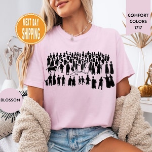 May include: Light pink t-shirt featuring a black graphic of a crowd of people. The shirt has the words "Comfort Colors 1717" printed on it. A round sticker says "Blossom" and another sticker says "Next Day Shipping".