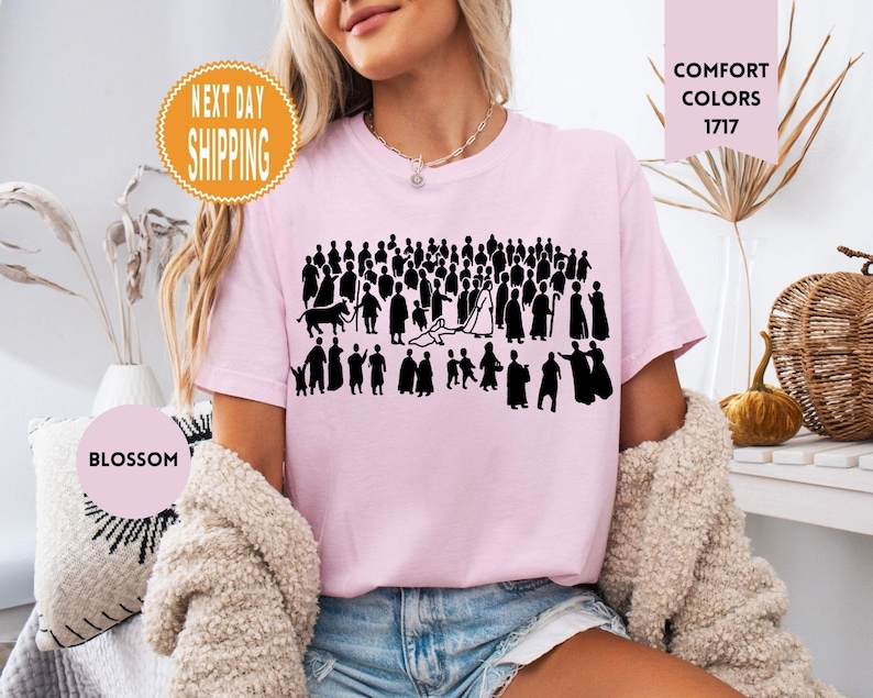 May include: Light pink t-shirt featuring a black graphic of a crowd of people. The shirt has the words "Comfort Colors 1717" printed on it. A round sticker says "Blossom" and another sticker says "Next Day Shipping".