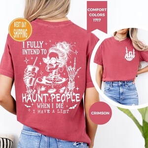 K&ouml;nnte beinhalten: Karmesinrotes T-Shirt mit wei&szlig;er Grafik eines Skeletts mit Brille, Getr&auml;nk und Handgeste. Der Text lautet: "I FULLY INTEND TO HAUNT PEOPLE WHEN I DIE I HAVE A LIST." Teil der Comfort Colors 1717 Kollektion.