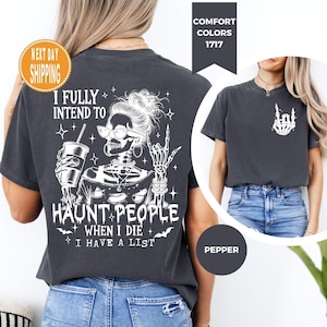 K&ouml;nnte beinhalten: Dunkelgraues T-Shirt mit einem wei&szlig;en Skelett-Motiv, das eine Sonnenbrille tr&auml;gt, ein Getr&auml;nk h&auml;lt und eine Handbewegung macht. Der Text lautet: "I FULLY INTEND TO HAUNT PEOPLE WHEN I DIE I HAVE A LIST".