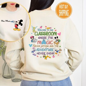 May include: A cream-colored sweatshirt with a Mickey Mouse design and the text "Welcome to our classroom where the magic never stops and the adventure never ends!" printed on the front.