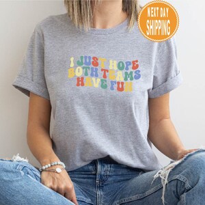 May include: Gray t-shirt with the text "I just hope both teams have fun" in rainbow colors.