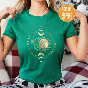 Op de afbeelding: Een groen T-shirt met een gouden ontwerp van een zon en maan met bloemmotieven. Het ontwerp is omringd door een cirkel van kleine manen.