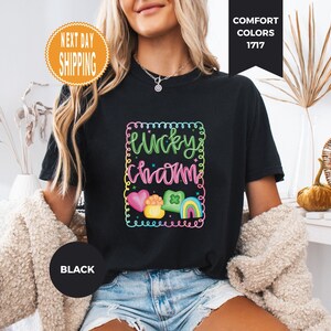 May include: Black t-shirt with a colorful "Lucky Charm" graphic. The design includes a heart, a pot of gold, a four-leaf clover, and a rainbow. The shirt is a Comfort Colors brand.