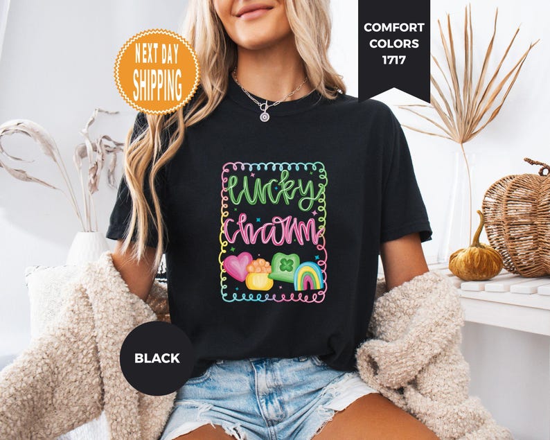 May include: Black t-shirt with a colorful "Lucky Charm" graphic. The design includes a heart, a pot of gold, a four-leaf clover, and a rainbow. The shirt is a Comfort Colors brand.
