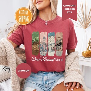 May include: Crimson-colored t-shirt featuring a graphic of Walt Disney World landmarks. The shirt has a crew neck and short sleeves. The words "Walt Disney World" are printed in white script below the graphic. The shirt is made of a soft material.