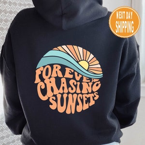Könnte beinhalten: Schwarzer Hoodie mit einem Grafikdruck eines Sonnenuntergangs und dem Text "FOREVER CHASING SUNSETS" in einer Retro-Schrift.
