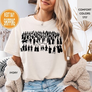 May include: Ivory-colored t-shirt featuring a black silhouette of a crowd of people. The shirt has the words "Comfort Colors 1717" printed on it. The shirt also has the words "Next Day Shipping" printed on it.