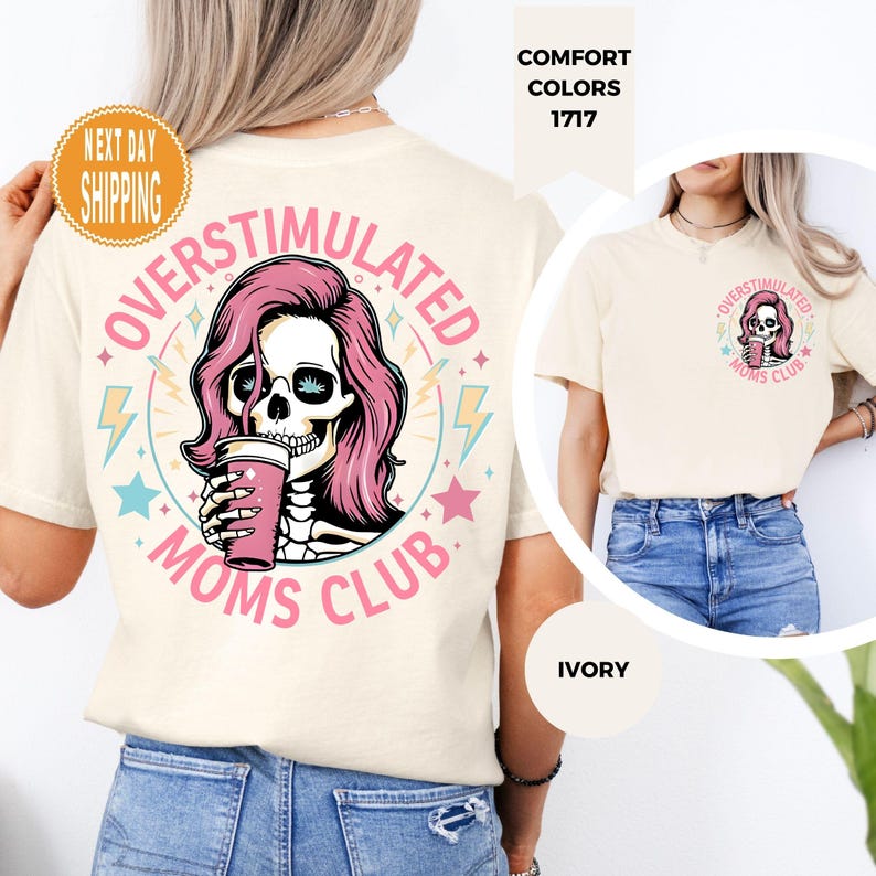 May include: Ivory-colored t-shirt featuring a graphic of a skull with pink hair holding a pink cup, surrounded by the words "OVERSTIMULATED MOMS CLUB." The design includes stars and lightning bolts. The shirt is a comfort color.