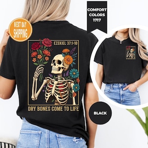 May include: Black t-shirt featuring a skeleton holding flowers, with text reading "Ezekiel 37:1-10" and "Dry Bones Come to Life." The design includes colorful flowers and a gold border. The shirt also has a small graphic on the upper back.