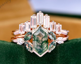 May include: A three-piece rose gold ring set with a moss agate center stone and baguette-cut diamonds. The moss agate is a green and brown gemstone with a unique pattern.