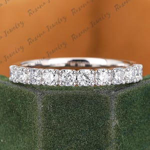 Pode incluir: Um anel de prata com uma fileira contínua de pequenas pedras preciosas redondas e transparentes. O anel é exibido em um fundo verde e dourado. O texto "Roxana Jewelry" é visível.