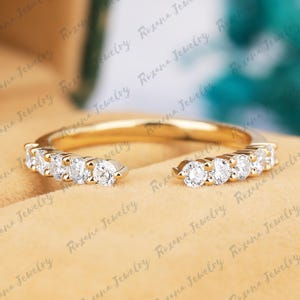 May include: A gold open-style ring featuring a row of small, round, clear stones set along each side of the band. The band is polished yellow gold, and the stones are arranged in a symmetrical pattern, leaving a gap at the top of the ring.