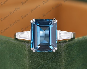May include: A silver ring with a large, rectangular, blue gemstone at its centre. Two smaller, rectangular, white gemstones are either side of the main stone. The ring is set against a green velvet surface.