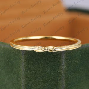 Puede incluir: Un anillo fino de oro amarillo pulido que presenta un delicado diseño trenzado en el centro. La banda tiene un perfil liso y redondeado con detalles milgrain finos a lo largo de los bordes, creando una textura sutil que capta la luz.