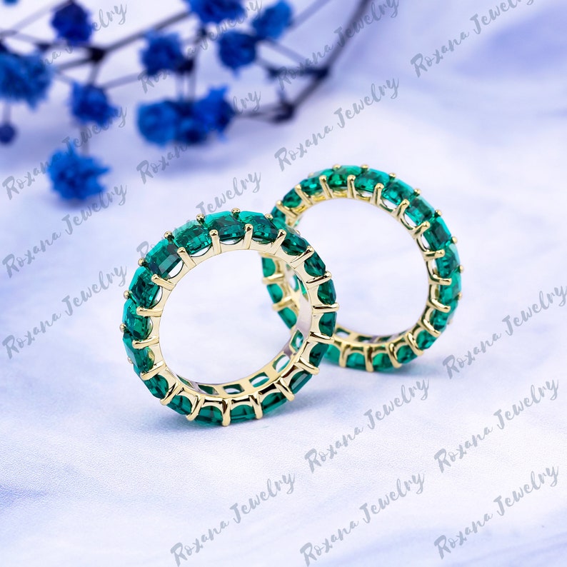 May include: Two gold rings with emerald green gemstones. The rings are set with a row of square-shaped stones.