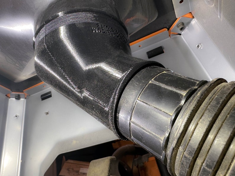 May include: Close-up of a black rubber hose connected to a black plastic pipe. The pipe has a ribbed texture and is connected to a larger, black, 3D printed pipe.