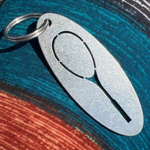 May include: A silver metal keychain with a cutout of a tennis racket. The keychain is oval shaped and has a silver ring.