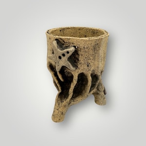 May include: A textured, beige-colored ceramic vase with a starfish design. The vase has a unique, organic shape with a rough, weathered appearance. The starfish is attached to the side of the vase. The vase is approximately 5 inches tall.